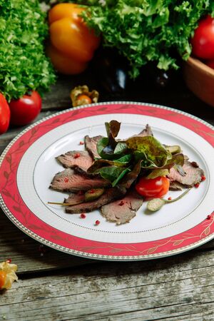 Restaurant dish with vegetable decor on a wooden background. Beef cut-up on a plate with greens. の写真素材
