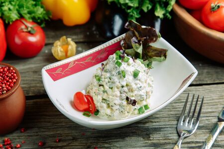 Restaurant dish with vegetable decor on a wooden background. Russian salad Olivier on a plate with herbs.の写真素材