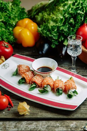 Restaurant dish with vegetable decor on a wooden background. Roll with salmon and greens on a plate.の写真素材