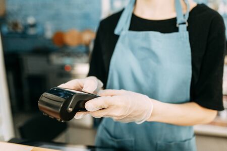 Precautions during quarantine. A gloved waiter with a cashless payment terminal.の写真素材
