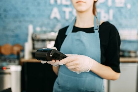 Precautions during quarantine. A gloved waiter with a cashless payment terminal.の写真素材