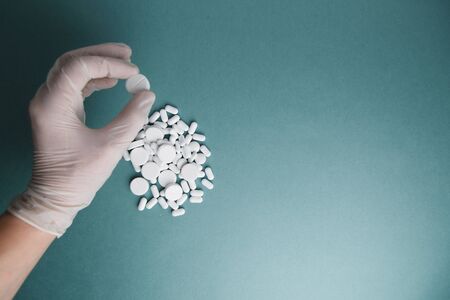 White tablets on a blue background are isolated. Layout of Flatley tablets. Gloved hand with a pill. Virus protection and 2019-ncov.の写真素材
