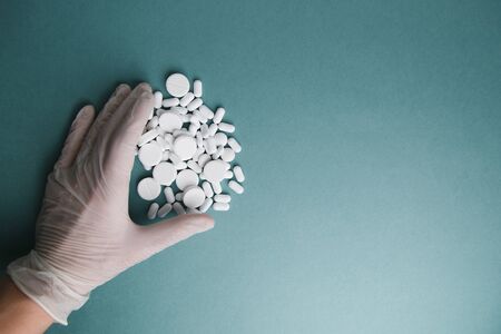 White tablets on a blue background are isolated. Layout of Flatley tablets. Gloved hand with a pill....