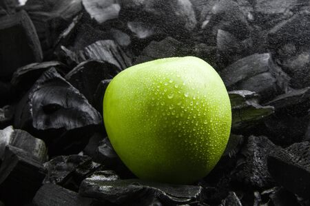 Fresh fruit on a dark texture. Splashes of water and drops in the air. Green ripe Apple with drops. Black charcoal background.の写真素材