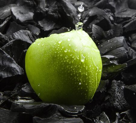Fresh fruit on a dark texture. Splashes of water and drops in the air. Green ripe Apple with drops. Black charcoal background.の写真素材