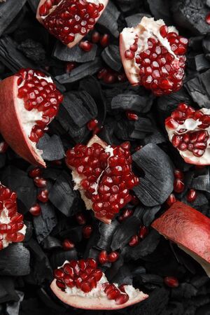 Red fruit slices on a dark texture. Preparation for hookah. Ripe cut pomegranate. Black charcoal background.の写真素材