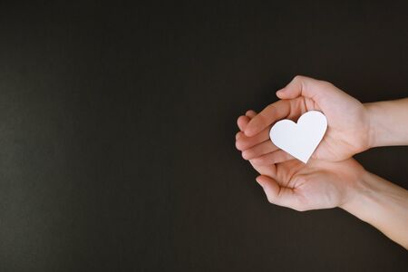 Black paper background. Paper heart. Hands palms up. の写真素材