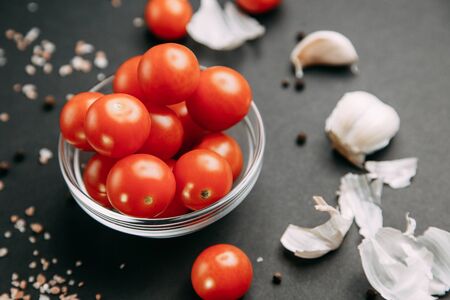Ingredients on black background. Cherry tomatoes with garlic and salt in bowls. の写真素材