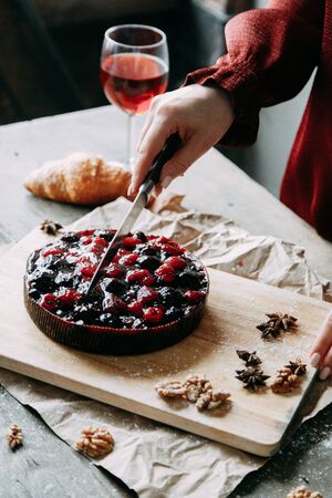 Hands of a cook girl with a knife. Berry cake on a wooden Board. Cutting raspberry and cherry pie. 