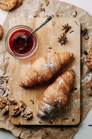 Flatley layout with nuts and powdered sugar. Croissants with raspberry jam. Fresh pastries on a wooden background. の写真素材