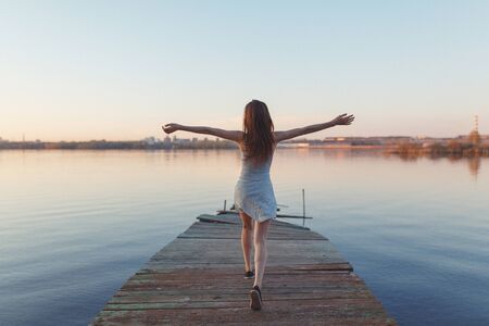 Summer Sunny walk along the beach. Emotional beautiful girl at sunset on the pier.の写真素材