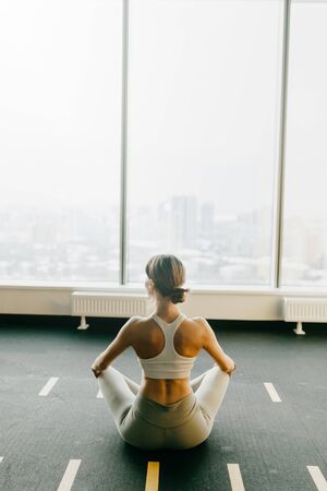 The girl is sitting on the Mat, relax. Exercises for self-control in yoga. Bright gym. Relaxed posture during meditation.の写真素材