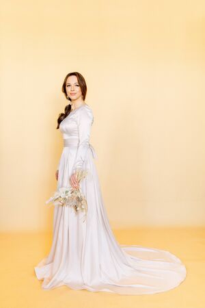 Girl in a wedding dress. Minimalism at a wedding photo shoot. Beautiful bride in the Studio on a yellow background.の写真素材
