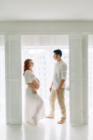 Pregnant woman in arms in white clothes. Happy couple waiting for a tropical baby.の写真素材