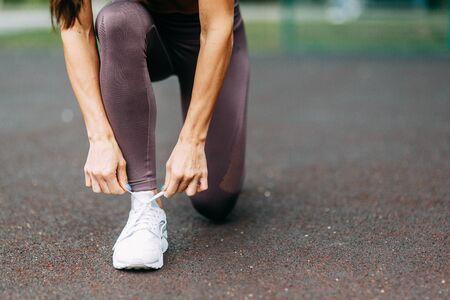  Feet and tying shoelaces sitting outside. Beautiful athletic girl on the Playground.の写真素材