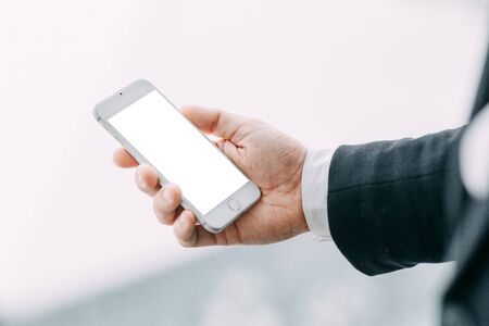 The phone in the hand of a business man, with a white screen. Blank for designers with bokeh.