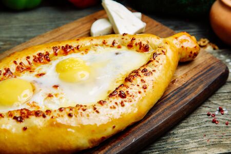 Azerbaijani restaurant dish with vegetable decor on a wooden background. Khachapuri in Adjarian on the Board.の写真素材