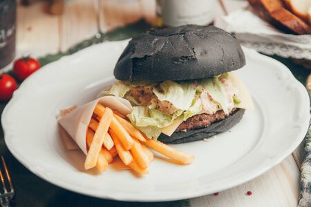 Beef cutlet with French fries. Burger with black bread on a wooden Board. 