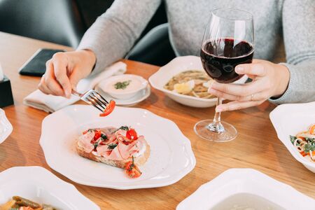 Restaurant dish on the menu with wine. The girl is eating bruschetta with bacon and tomato. 