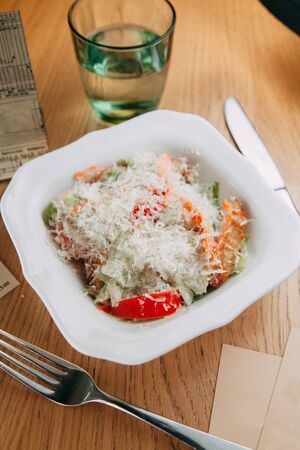Restaurant serving salad with cheese, tomatoes and herbs. Fresh vegetable salad on a white plate. 