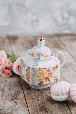 tea set in composition with flowers and marshmallows. Coffee mug on a saucer, a teapot and a sugar bowl. Filmed in the interiorの写真素材
