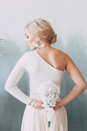 Beautiful bride in front of wedding arch with flowers and decor. Bouquet in the hands and details. The girl is happy, smiling and dancing. Dream wedding dress in modern styleの写真素材