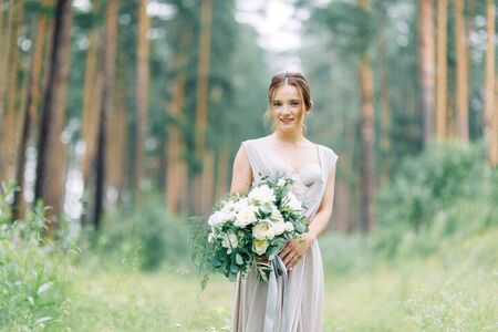 Boudoir photo shoot of the bride in the woods with a bouquet. Flying dress and beautiful girl in the Park.の写真素材