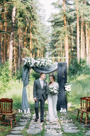 Wedding ceremony at the arch with pine forest in the style of fine art. Beautiful couple and traditions at a wedding in Europe.の写真素材