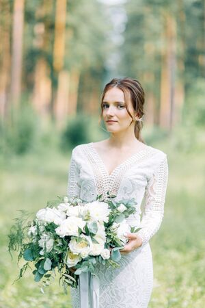 The bride in a wedding dress in nature with a bouquet. Boudoir photo shoot in pine lemu in the style of fine art.の写真素材