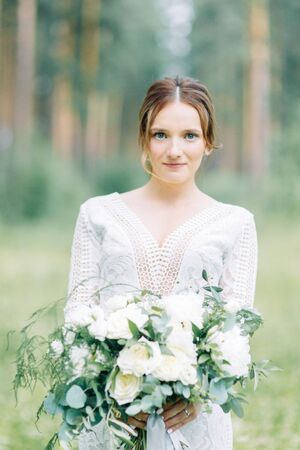 The bride in a wedding dress in nature with a bouquet. Boudoir photo shoot in pine lemu in the style of fine art.の写真素材