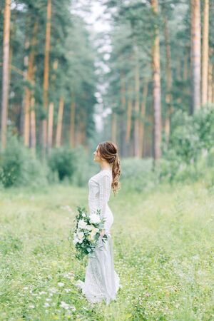 The bride in a wedding dress in nature with a bouquet. Boudoir photo shoot in pine lemu in the style of fine art.の写真素材