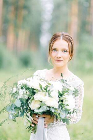 The bride in a wedding dress in nature with a bouquet. Boudoir photo shoot in pine lemu in the style of fine art.の写真素材