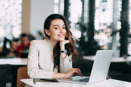 Beautiful Russian business girl working on laptop, smiling and typing on the keyboard. Working time, business image and a job in a cafeの写真素材
