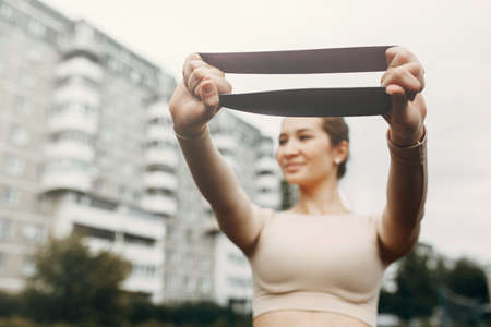 A beautiful girl with a smile is flexing her muscles. Stretches, trains with an elastic band for stretching.の写真素材