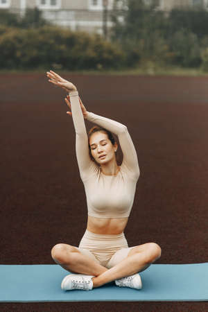 Beautiful woman relaxing yoga at the stadium. Training and stretching on the gym Mat.