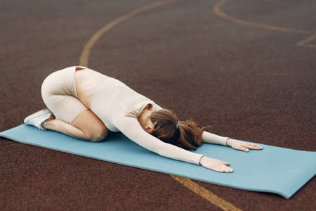 Athletic girl on the Mat is warming up. Training at the stadium with stretching.