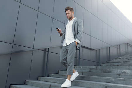 The businessman smiles and listens to music with headphones. A young man on the street with a phone in his hands.の写真素材
