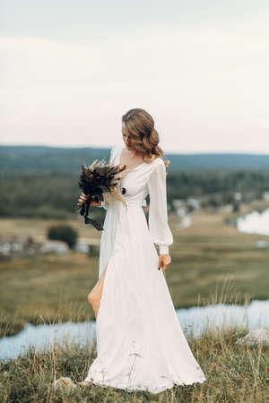 Bride with a bouquet of dried flowers walking in nature. Boho style wedding in autumn.の写真素材