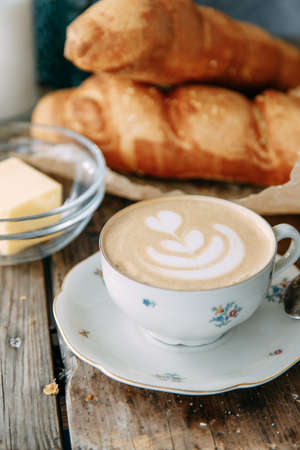 Breakfast with a buttered bun and a Cup of coffee. Cappuccino coffee on a wooden table with a loaf of bread.の写真素材