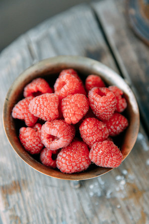 A pile of raspberries in a metal plate with a blurry background. Ripe raspberries close-up on a wooden table.の写真素材