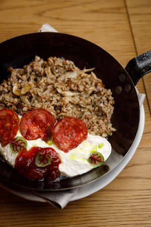 Dish in a frying pan close-up. Boiled buckwheat with mushrooms and tomatoes on a wooden background.の写真素材