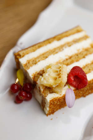 A piece of cake close-up on a plate. Cake with cream and strawberries on a dark wood background.の写真素材