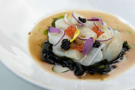 Restaurant dish close-up, decorated with fresh flowers. Sea salad with scallops and red caviar, on a white plate.の写真素材