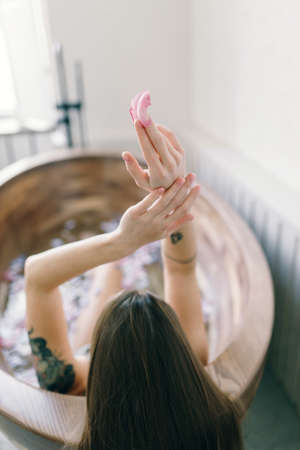 An attractive naked girl enjoys a bath with milk and rose petals. Spa treatments for skin rejuvenation.の写真素材