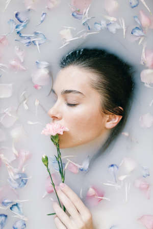 A sensual portrait of a woman in a bath with milk and flowers. Spa treatments, soft skin and soft pastel shades.の写真素材