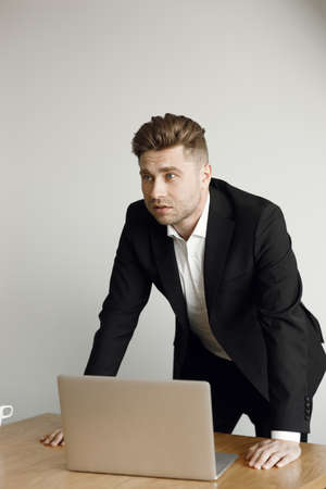 A man sits at a table and works with a cup of coffee. A handsome businessman working with a laptop in the office.の写真素材