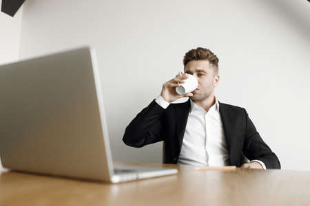 A man sits at a table and works with a cup of coffee. A handsome businessman working with a laptop...