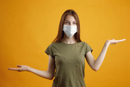 A medical theme with an empty background. Studio profile portrait of a young blonde in a medical flu mask on a yellow background with a copy space.の写真素材