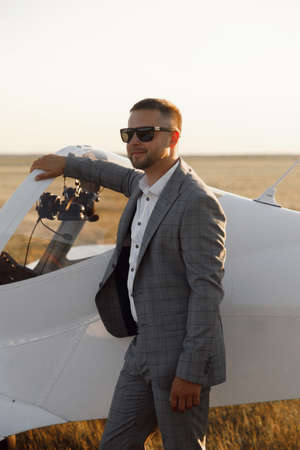 A male pilot, against the background of an airplane at sunset. The groom in a suit is standing near his private plane.の写真素材