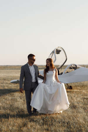 A couple on the background of a private plane at sunset. A sensual wedding couple, the bride and groom are standing together next to the plane.の写真素材